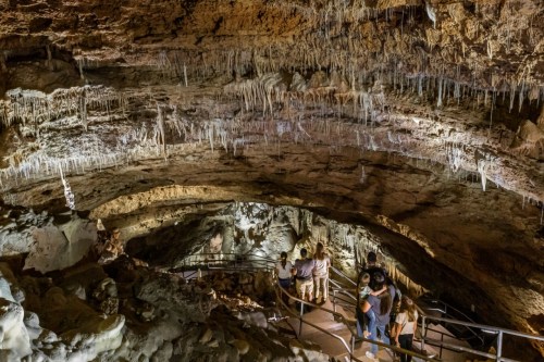 Visitors explore a cave with stalactites hanging from the ceiling and a winding path leading through the rocky terrain.
