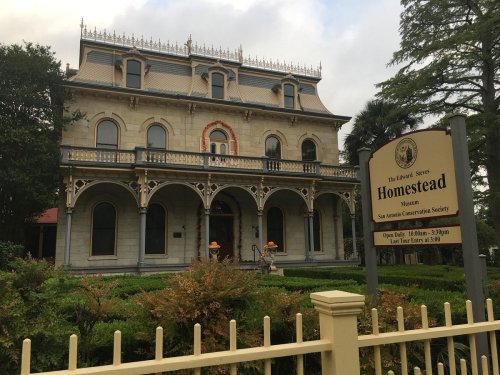 Historic Homestead Museum with ornate architecture, surrounded by greenery and a sign detailing visiting hours.