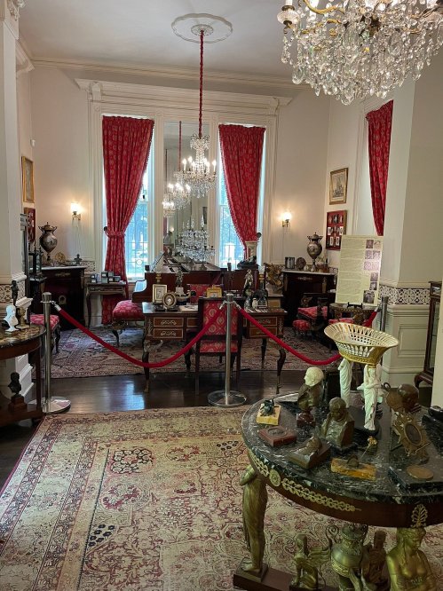 A vintage room with ornate furniture, chandeliers, and decorative items, featuring red curtains and a patterned rug.
