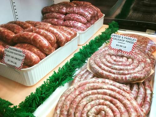 Display of handmade Italian sausages and cheese & parsley sausage rings in a market setting.