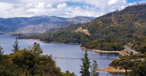 A scenic view of a lake surrounded by mountains and trees under a partly cloudy sky.