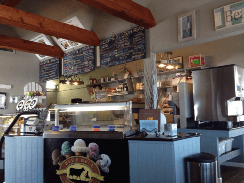 Interior of a cozy ice cream shop with a display case, menu boards, and wooden beams overhead.
