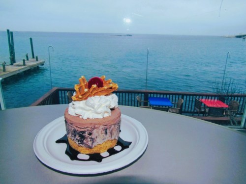 A dessert with chocolate ice cream, whipped cream, and a cherry sits on a table with a view of the ocean.