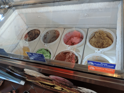 A display of various ice cream flavors in tubs, including chocolate, mint, and rainbow sherbet.