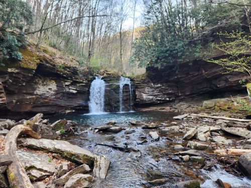 A serene waterfall cascades into a rocky pool, surrounded by lush greenery and steep, moss-covered cliffs.