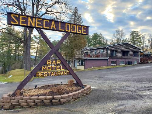 Sign for Seneca Lodge with bar, motel, and restaurant; rustic building and trees in the background under a cloudy sky.