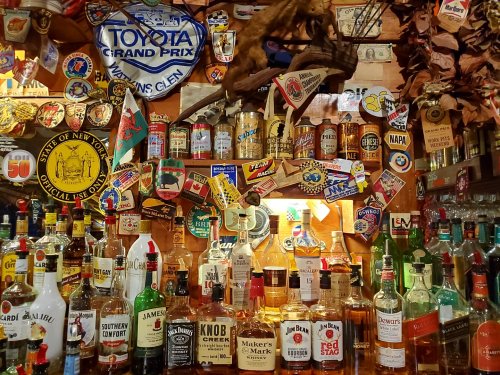 A vibrant bar display featuring various liquor bottles, vintage signs, and memorabilia on a wooden backdrop.