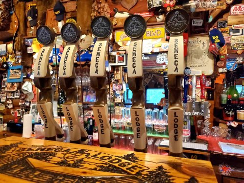 Five beer taps labeled "Seneca Lodge" in a rustic bar setting with various memorabilia in the background.