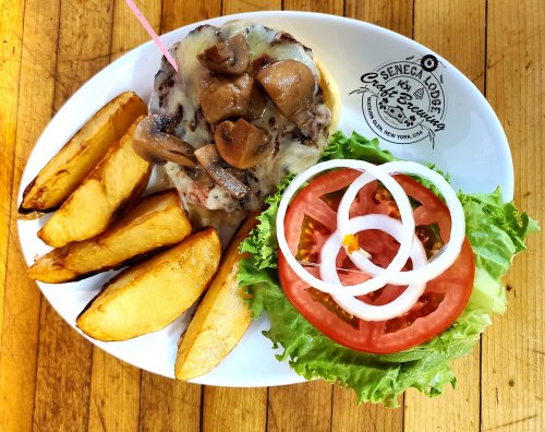 A plate with a cheeseburger topped with mushrooms, lettuce, tomato, and onion, alongside golden potato wedges.