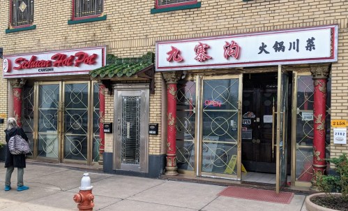 A person stands outside a restaurant with two entrances, one labeled "Sichuan Hot Pot" and the other with Chinese characters.