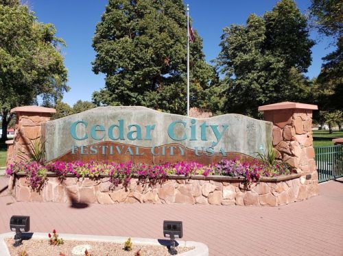 Sign for Cedar City, Festival City USA, surrounded by flowers and trees on a sunny day.