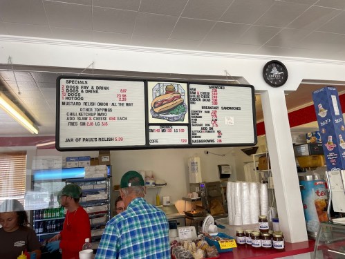 Menu board displaying specials and prices for hot dogs, drinks, and breakfast sandwiches in a casual eatery.