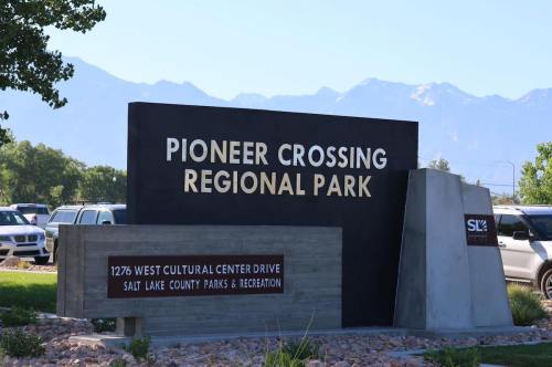 Sign for Pioneer Crossing Regional Park, featuring park name and address, with mountains in the background.