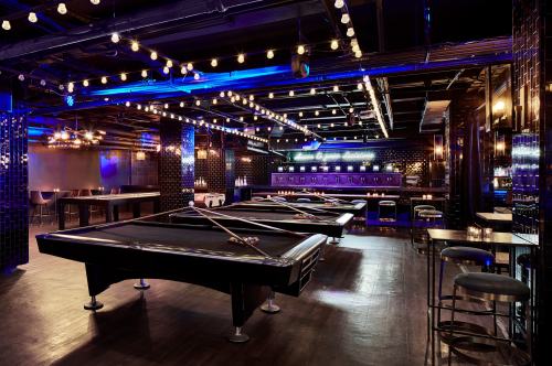 A stylish pool hall with multiple tables, dim lighting, and decorative string lights.