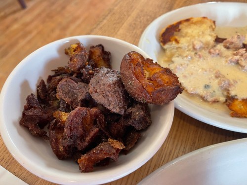 A bowl of crispy fried plantains next to a plate of creamy dish with chunks of meat and bread.