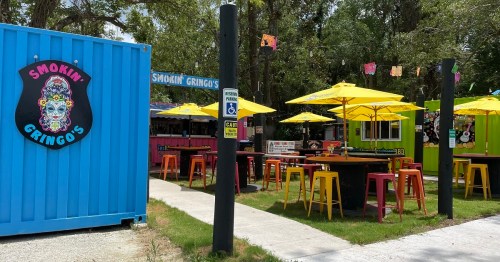 Colorful outdoor dining area with yellow umbrellas, tables, and food trucks at Smokin' Gringo's.