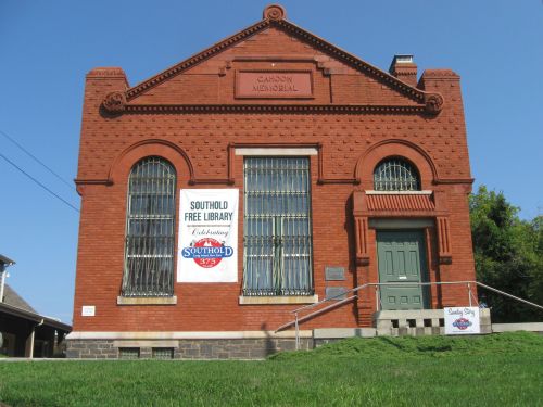 Red brick building with large windows, featuring a sign for Southhold Free Library and a ramp leading to the entrance.