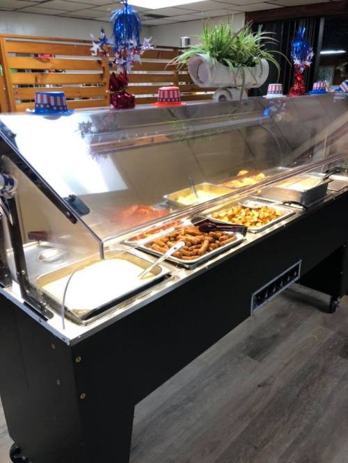 A buffet station with various food trays under a glass cover, decorated with festive red, white, and blue accents.