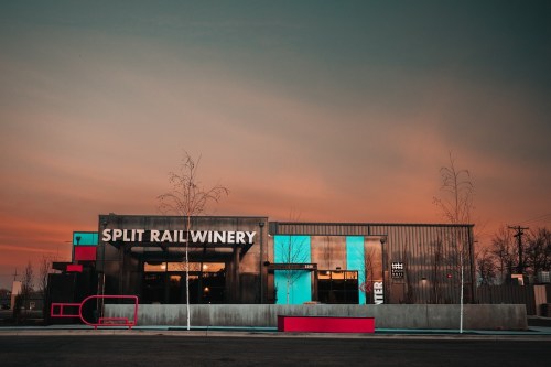 Modern winery building with a sleek design, featuring colorful accents and a sunset sky in the background.