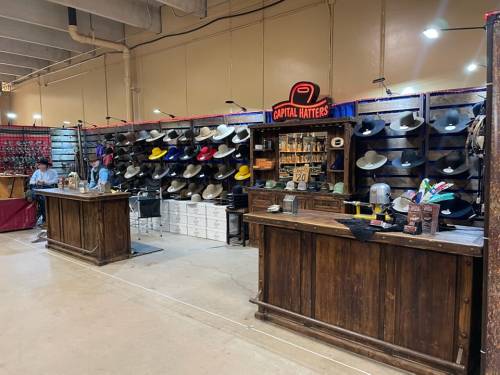 A rustic booth displaying various colorful hats, with wooden counters and a sign reading "Capital Hatters."