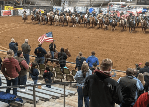 A rodeo scene with riders on horseback, an audience watching, and a person holding an American flag.