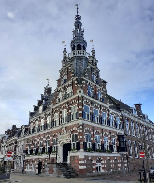 Historic building with ornate architecture, featuring a tall spire and decorative brickwork against a cloudy sky.