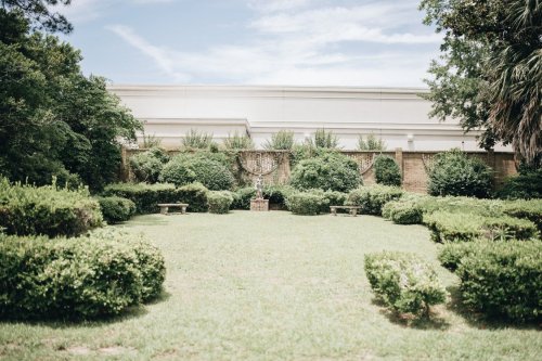 A serene garden with neatly trimmed hedges, benches, and a backdrop of greenery under a clear sky.