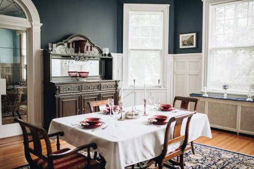 A dining room with a wooden table set for a meal, featuring elegant tableware and a dark wooden sideboard against a blue wall.