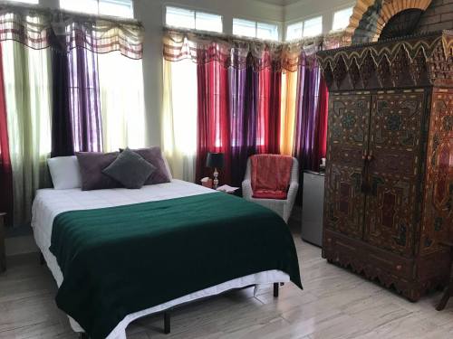 A cozy bedroom featuring a bed with a green blanket, colorful curtains, and an ornate wooden wardrobe.