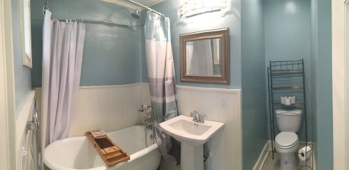 A cozy bathroom featuring a freestanding tub, pedestal sink, and light blue walls with a mirror and towel rack.
