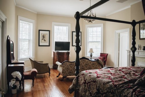 A cozy bedroom with a four-poster bed, vintage furniture, and large windows letting in natural light.