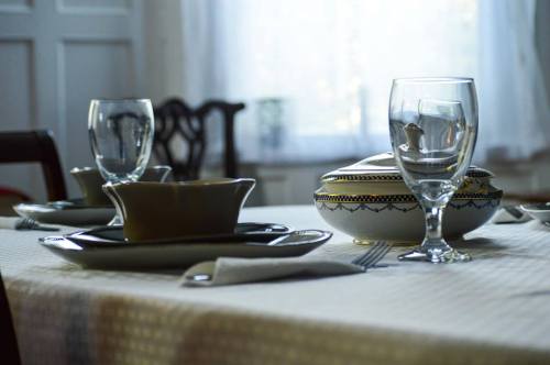 A beautifully set dining table with plates, glasses, and a decorative bowl, illuminated by natural light.