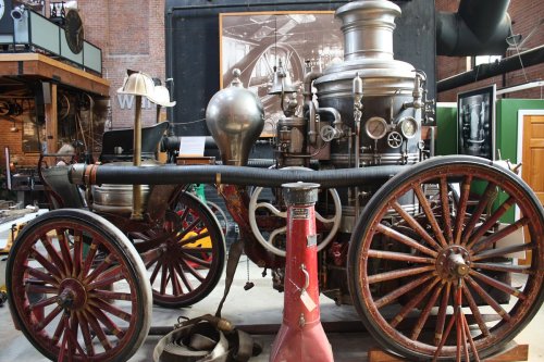 A vintage steam fire engine with large wheels and metal components, displayed in a museum setting.