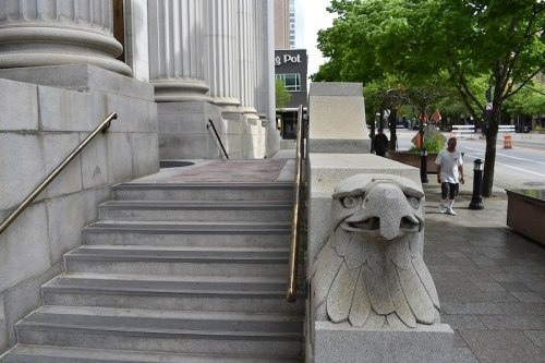 Stone steps lead up to a building, featuring a decorative eagle sculpture on the side and trees lining the street.