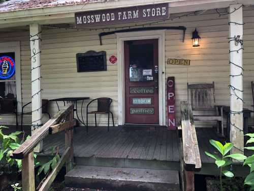 A rustic farm store entrance with a sign reading "Mosswood Farm Store," featuring outdoor seating and an "Open" sign.