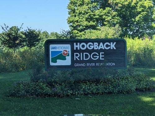 Sign for Hogback Ridge at Grand River Reservation, featuring greenery and flowers in the foreground.