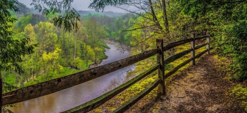 A scenic view of a river surrounded by lush greenery, with a wooden fence along a winding path.
