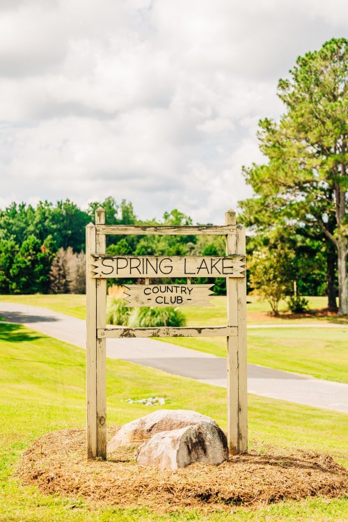 Sign for Spring Lake Country Club, surrounded by green grass and trees under a partly cloudy sky.