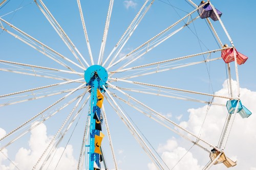 A colorful ferris wheel against a blue sky with fluffy clouds, featuring several empty gondolas.