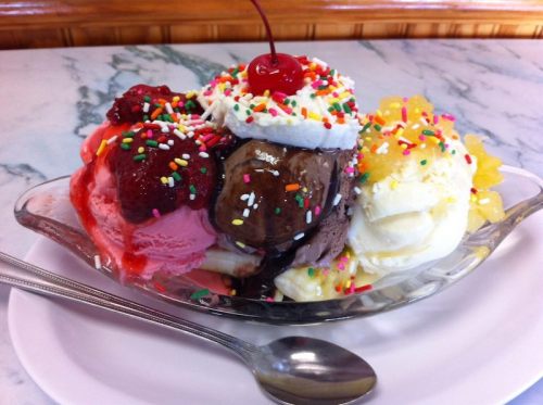 A colorful ice cream sundae with scoops of chocolate, strawberry, and vanilla, topped with whipped cream, sprinkles, and a cherry.