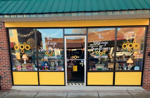 A storefront with large windows displaying colorful vintage items and sunflower decorations, labeled "The Vintage Sunflower."