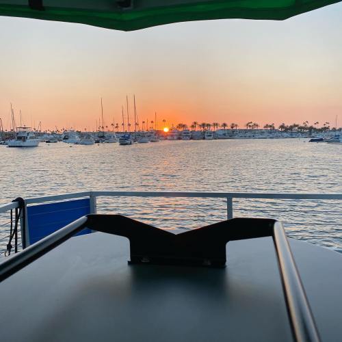 A serene sunset over a marina filled with boats, viewed from a deck with a green canopy.