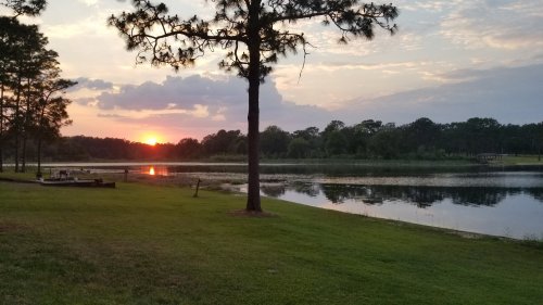 A serene lake at sunset, with trees lining the shore and a colorful sky reflecting on the water's surface.