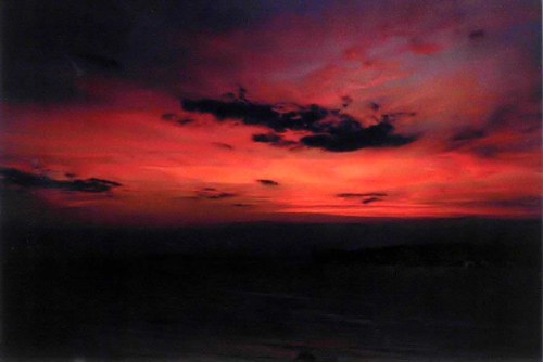 A vibrant sunset with deep reds and purples, featuring scattered clouds against a darkening sky.