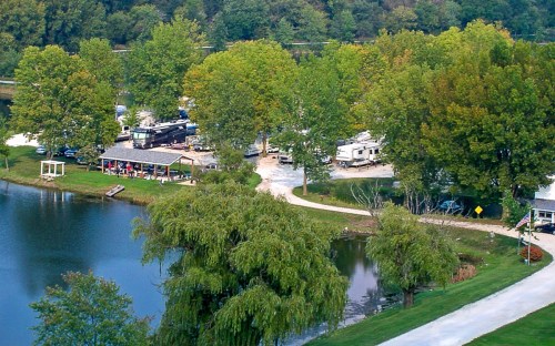 Aerial view of a serene lakeside area with trees, a campground, and a winding path beside the water.