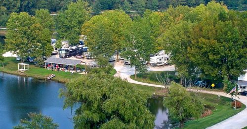 Aerial view of a serene lakeside area with trees, a campground, and a winding path beside the water.