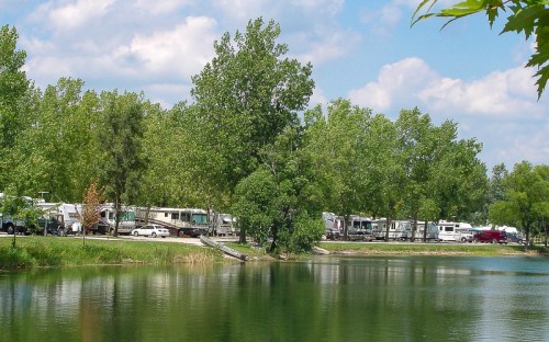 A serene lake scene with RVs parked along a tree-lined shore under a partly cloudy sky.