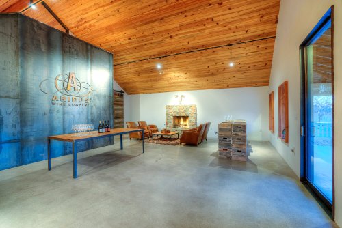 Interior of a modern wine tasting room with a wooden ceiling, fireplace, and a table set with wine glasses.