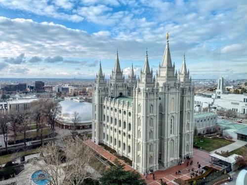 A grand temple with spires, surrounded by gardens and buildings, under a cloudy sky in a city landscape.