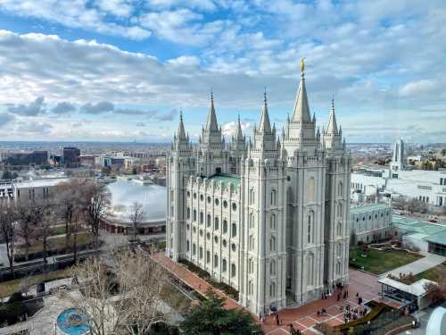 A grand temple with spires, surrounded by gardens and buildings, under a cloudy sky in a city landscape.